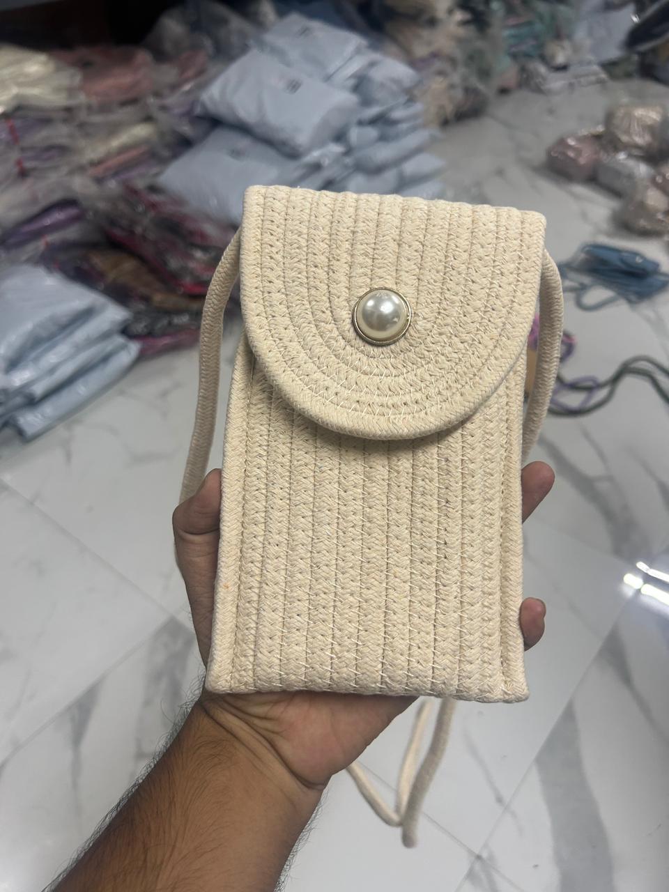 Cream braided crossbody phone bag with pearl button flap closure, held in hand.