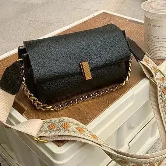 Close-up of the black TRENDBUY sling bag, highlighting its pebbled PU leather texture, gold-tone clasp, and a vibrant patterned broad strap.