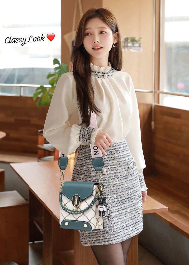 Young woman with long hair, wearing a white high-neck blouse and a tweed skirt, posing with the TRENDBUY teal and white broad belt sling bag as a crossbody.