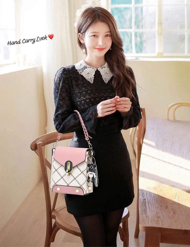 Woman in a black dress with a lace collar, holding the TRENDBUY pink and white broad belt sling bag by its short chain strap, demonstrating a hand-carry style.