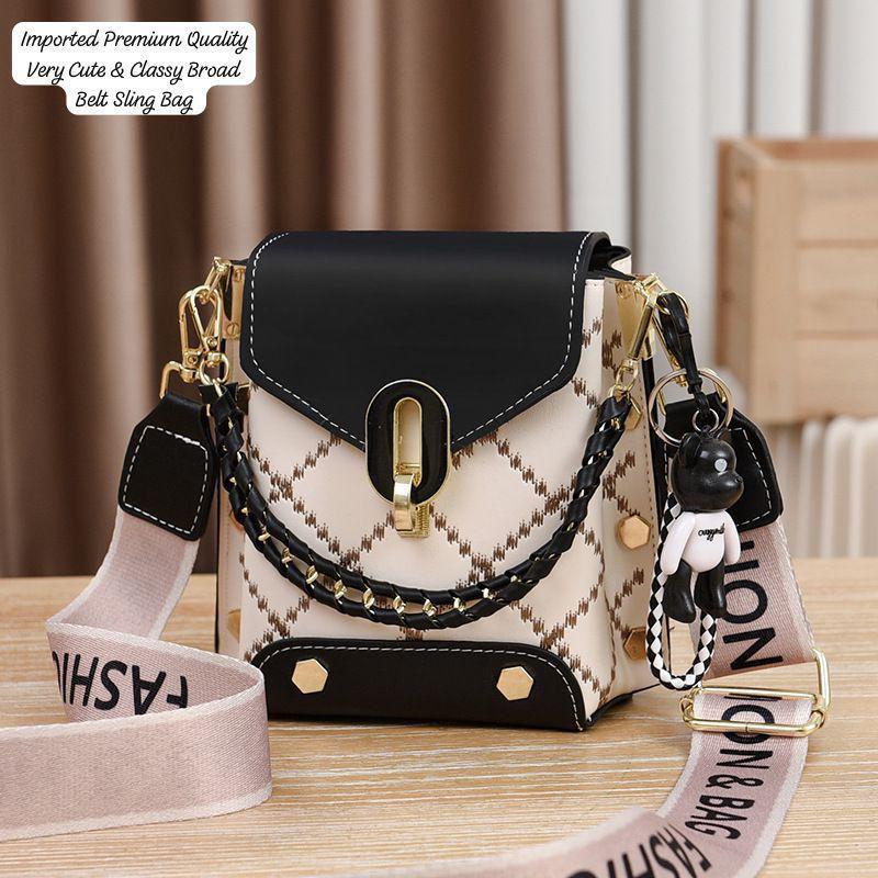 Stylish TRENDBUY black and white broad belt sling bag, featuring gold stud details, a decorative chain, and a black teddy bear keychain.