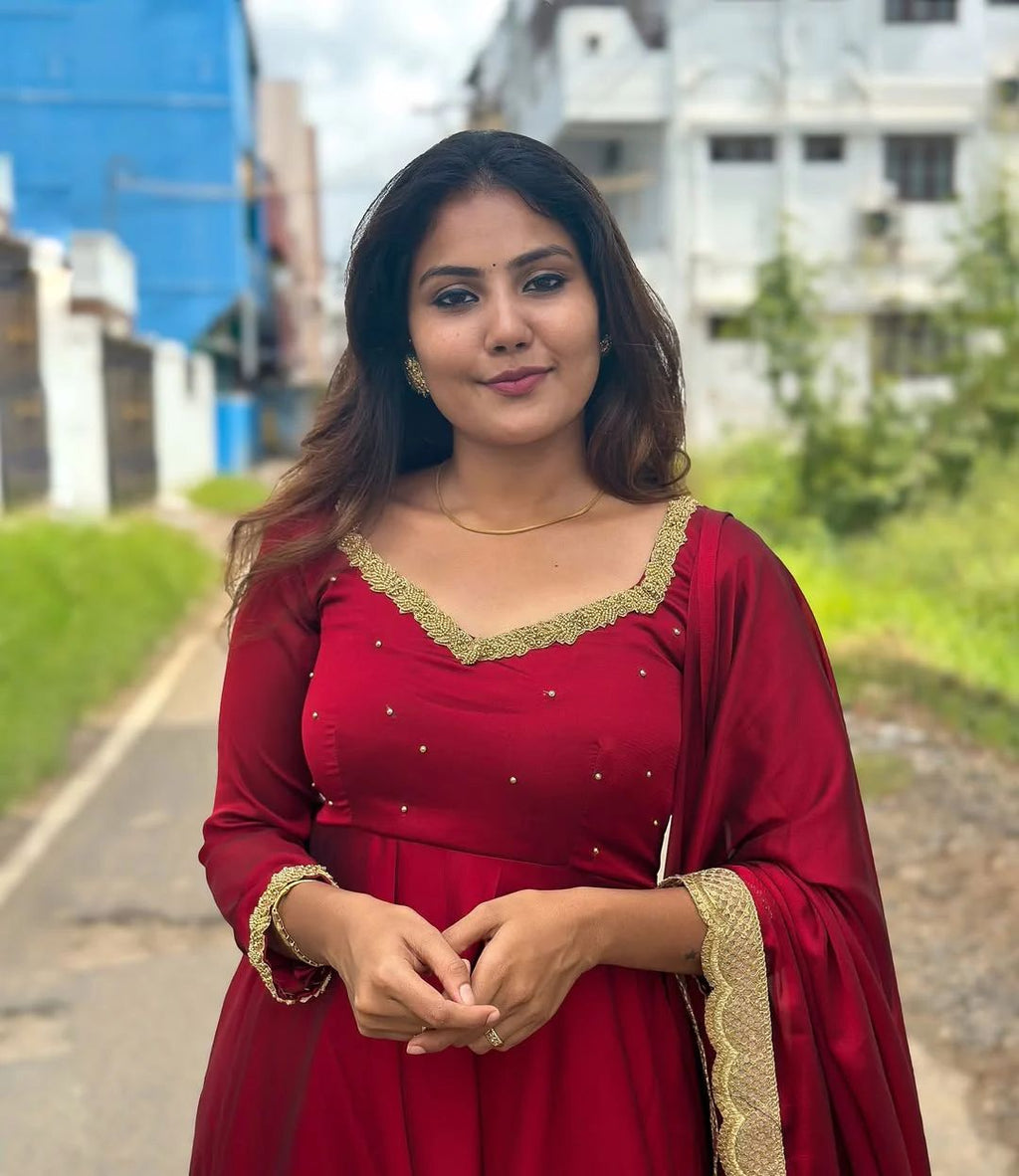 Woman wearing a red Sparkling Georgette Anarkali dress with golden embroidery on yoke, outdoors.