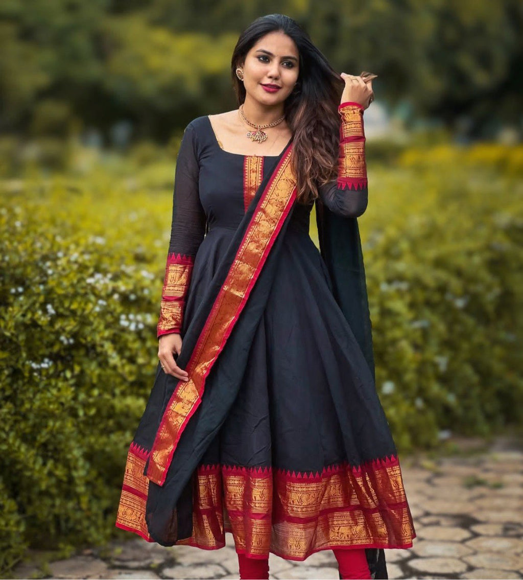 Woman wearing elegant black Anarkali kurti with red Pattu Zari border and dupatta, posing in a garden.