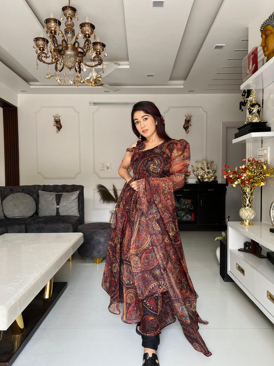 TRENDBUY woman models a paisley print organza anarkali suit with a huge flair in a stylish living room setting.