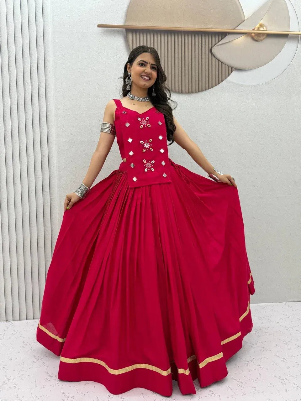 Front view of smiling model wearing a magenta cotton lehenga choli set featuring mirror work and gold border