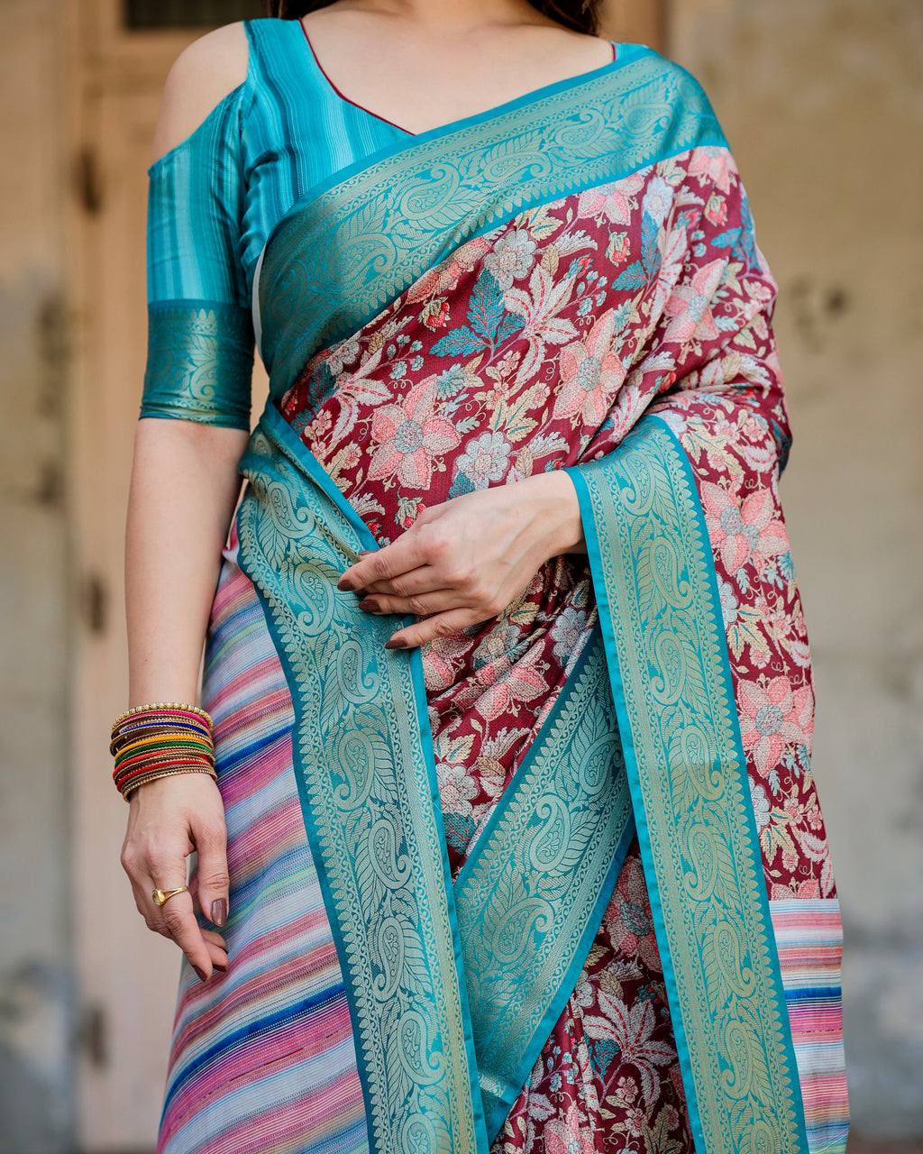 Close-up view of the Maroon and Teal Banarasi Silk Saree, highlighting the detailed floral patterns on the maroon base and the ornate teal zari border with paisley designs.
