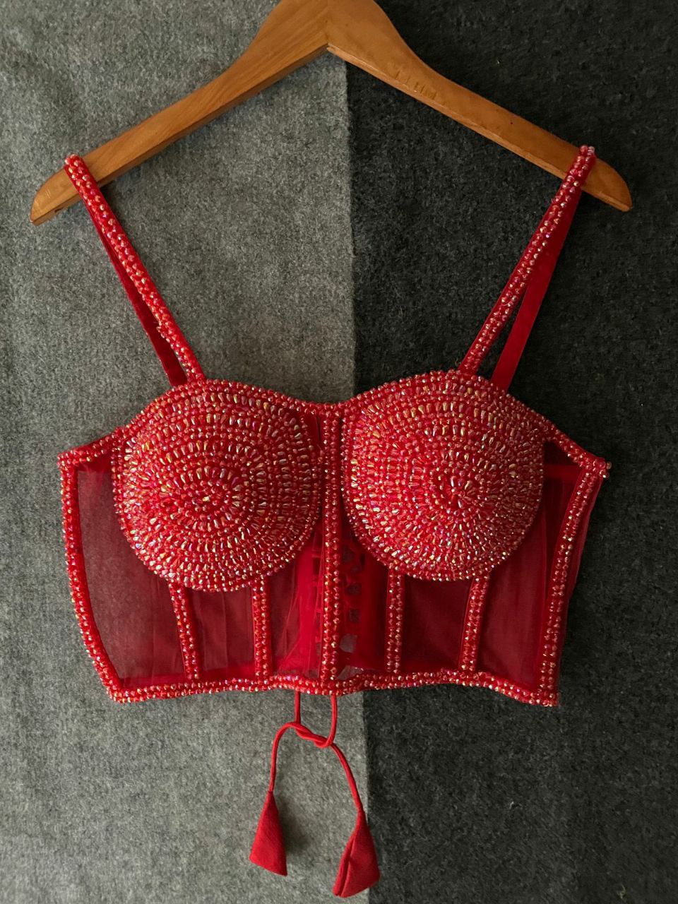 Red heavily beaded sleeveless corset blouse for women, front view, hanging on a wooden hanger.