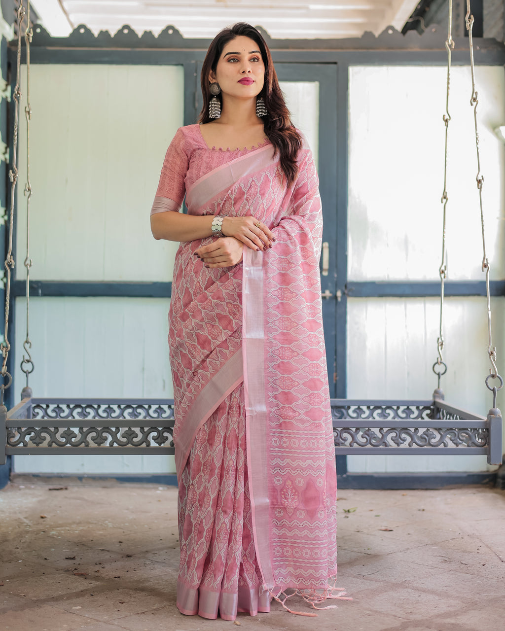 Elegant woman posing in a blush pink pure linen saree with intricate white embroidery, front view.