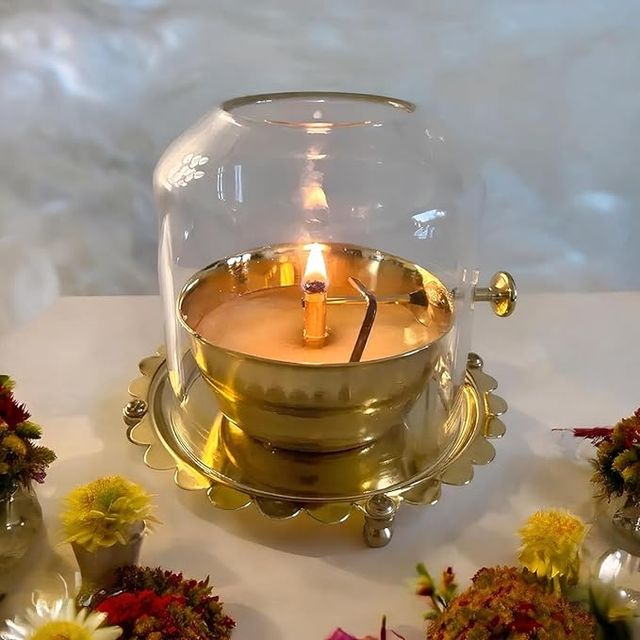Glowing Akhand Diya lamp made of clear glass with adjustable wick.