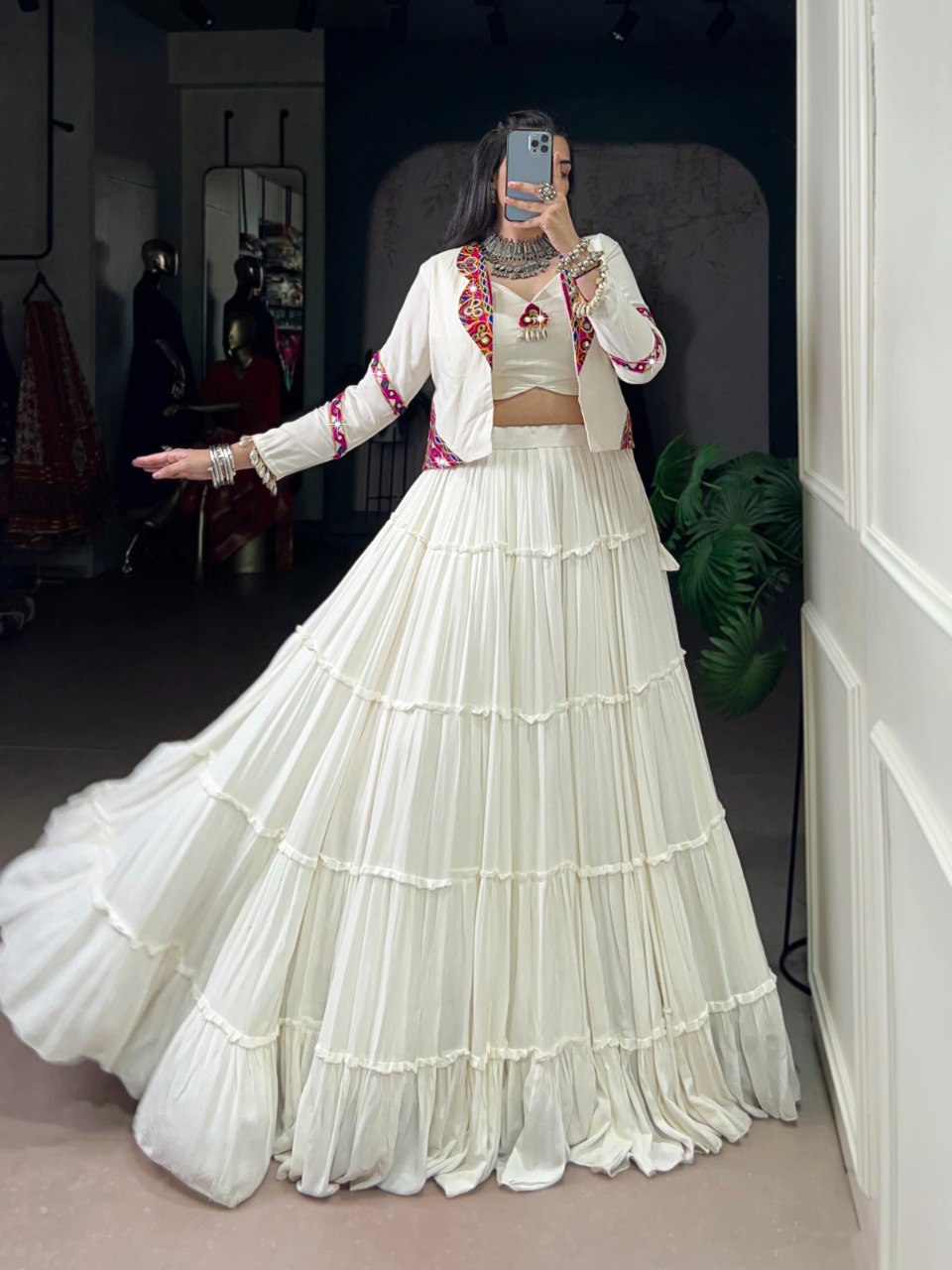 Woman posing in a white tiered rayon co-ord set lehenga with a white Koti jacket featuring colorful Gamthi mirror work and cowrie lace details.