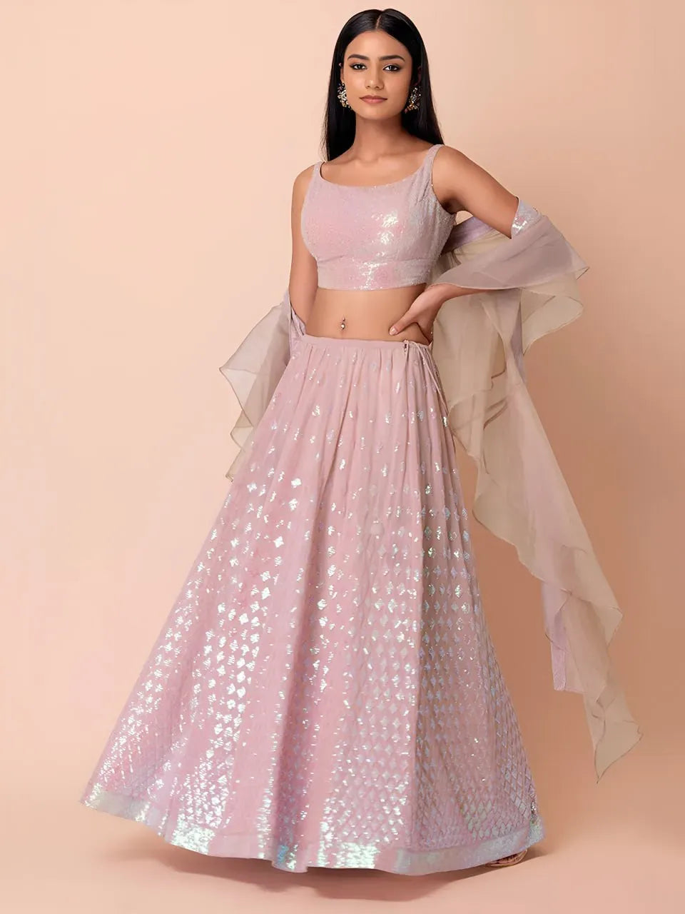 Model wearing blush pink sequin lehenga with sleeveless blouse and sheer ruffled dupatta