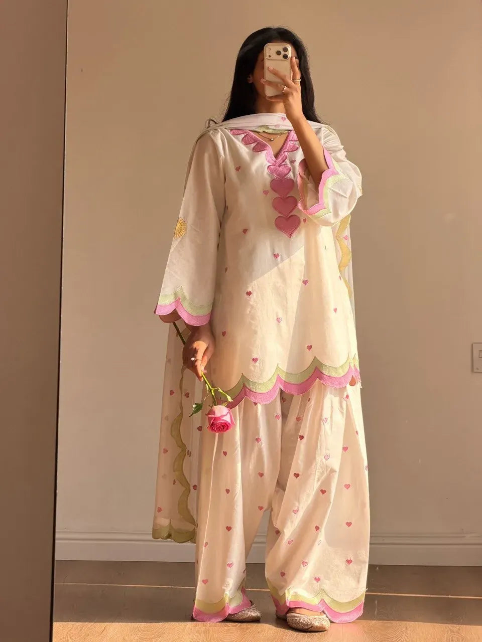 Model wearing white embroidered Chanderi salwar suit with pink heart details holding a rose
