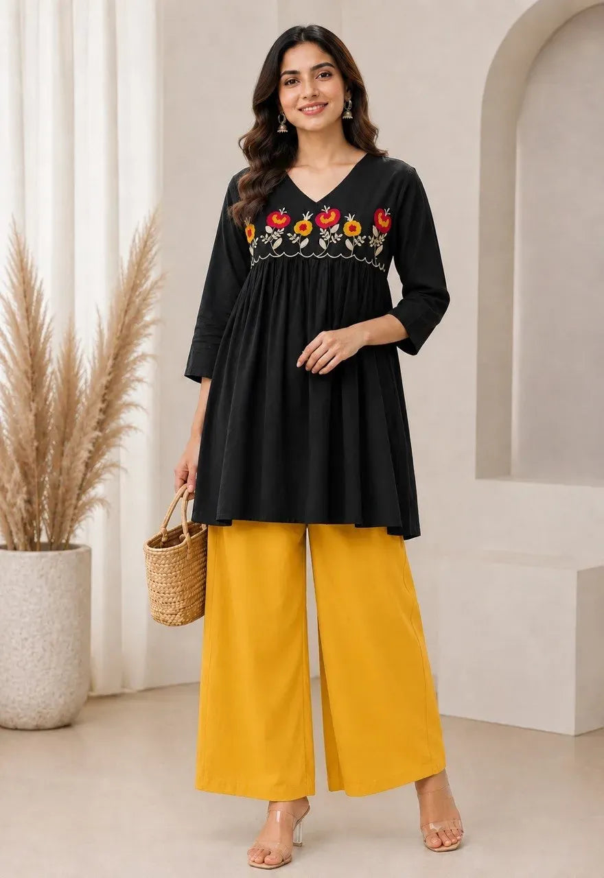 Front view of model in black tunic and yellow palazzo set standing indoors