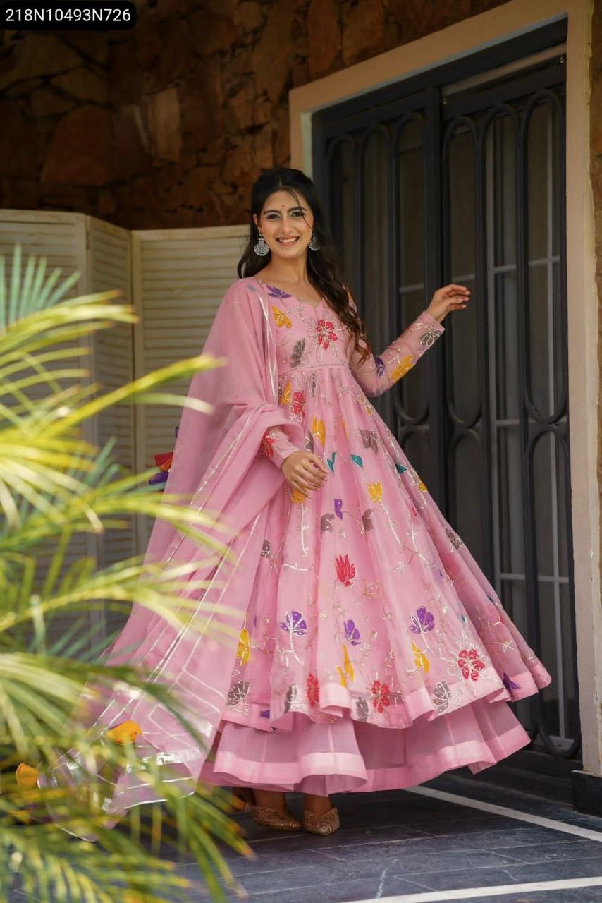 Full shot of model in pink embroidered georgette gown and sharara set, posing outdoors near a door and plants.