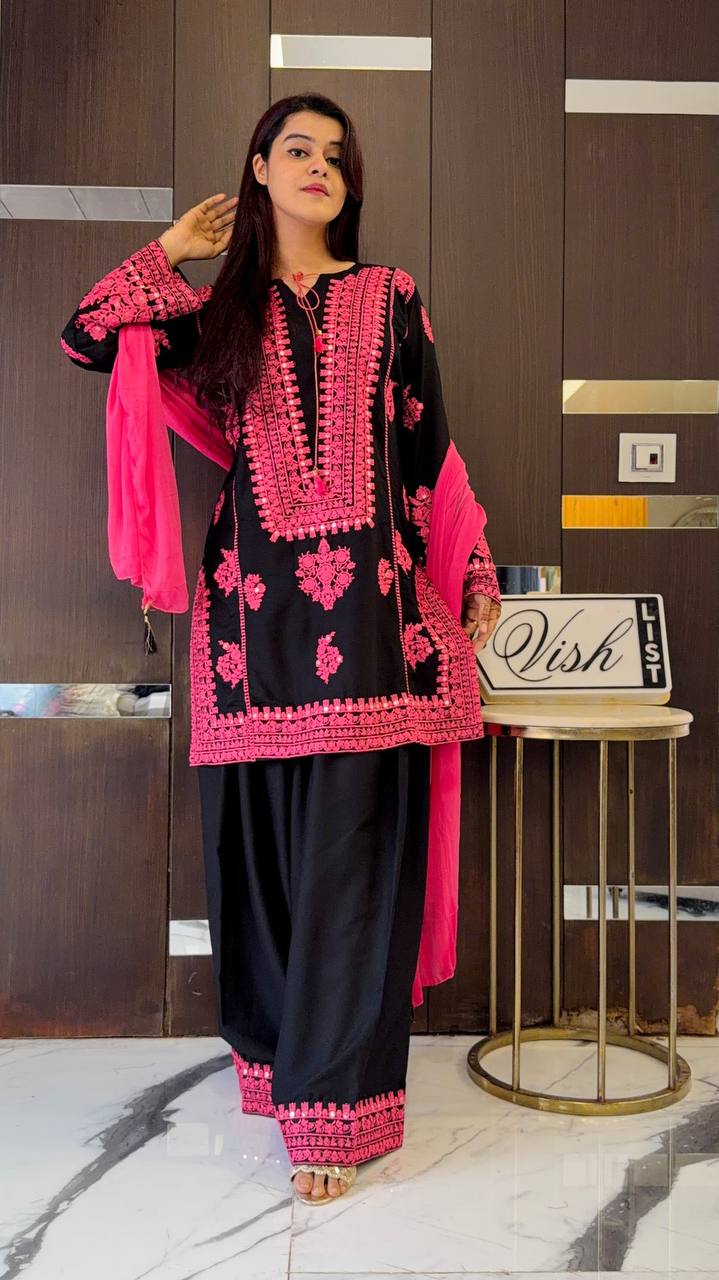 Woman posing in a black natural crepe silk suit with pink embroidery and mirror work, paired with a matching pink faux georgette dupatta.