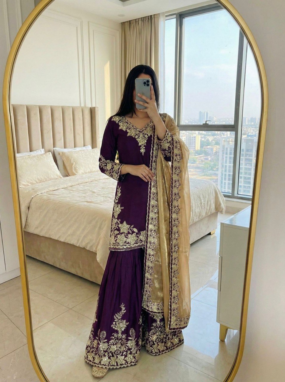 Woman in deep purple embroidered sharara suit with golden dupatta, mirror selfie.