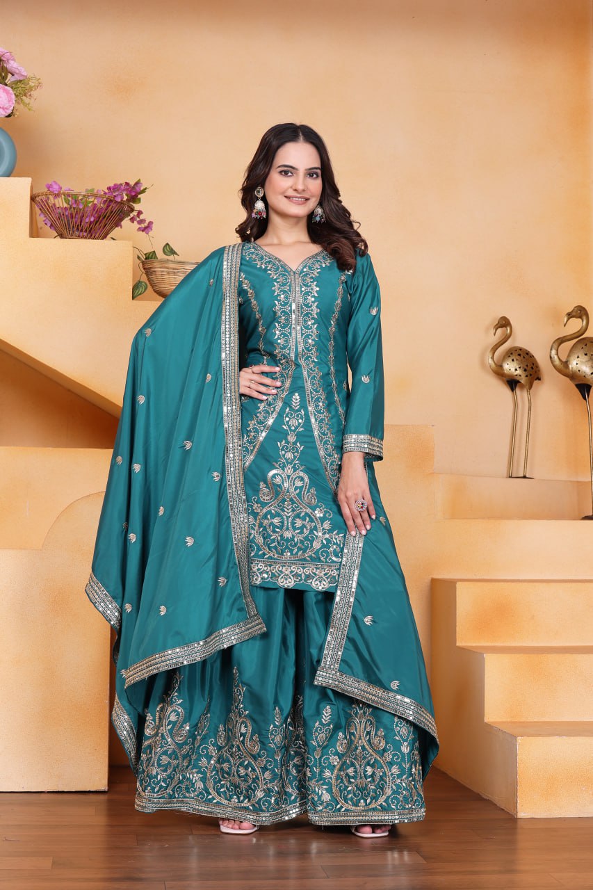 Full body shot of model wearing teal embroidered sharara suit, smiling, standing in an elegant setting.