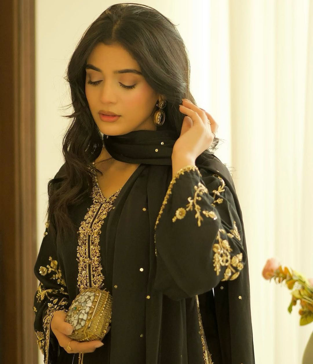 Woman in black georgette kurti set with golden embroidery and sequence work, holding a clutch, elegant close-up.
