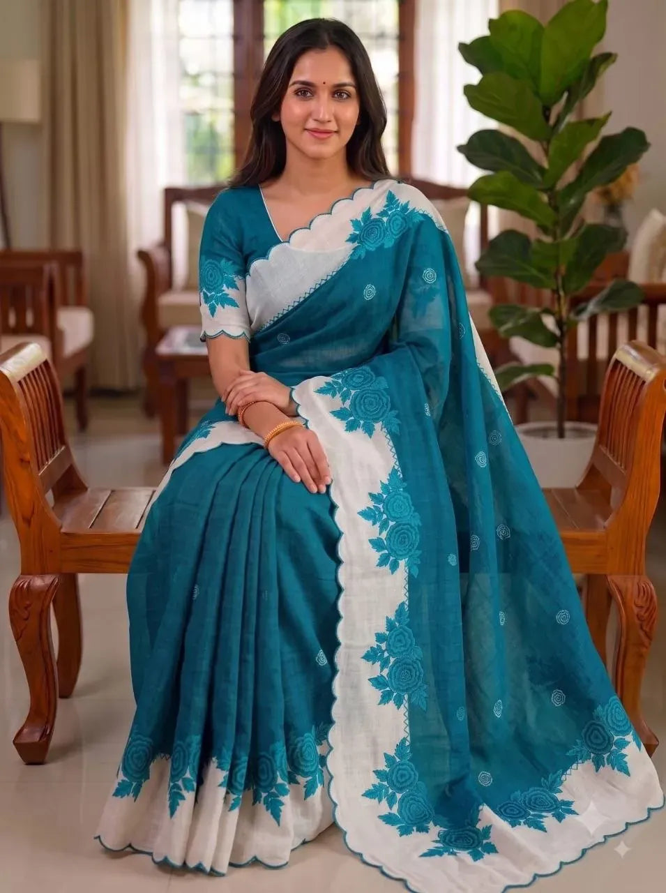 Model sitting wearing teal blue plain linen saree with white cut work border and digital print