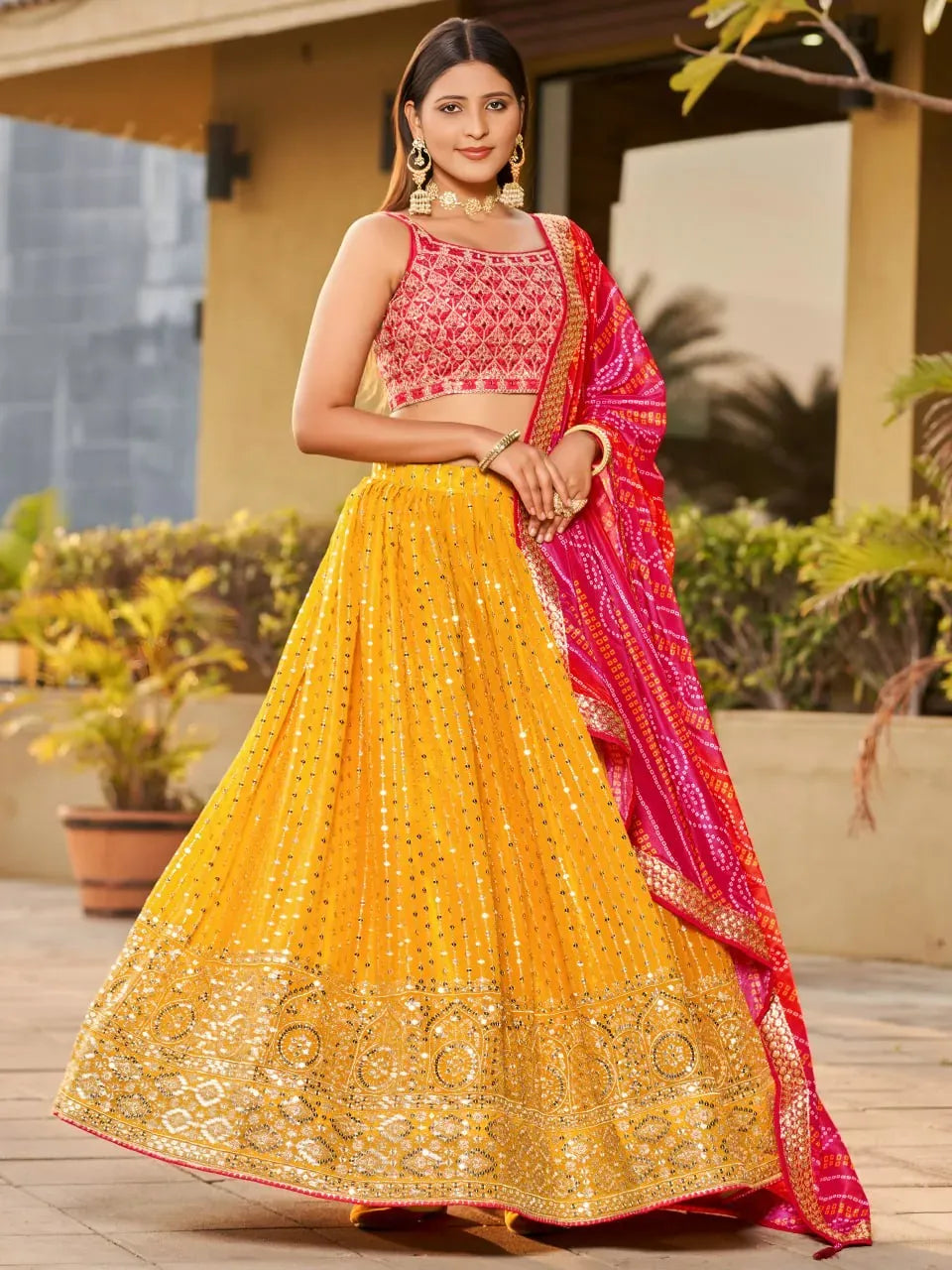 Model wearing mustard yellow georgette lehenga with red blouse and pink dupatta