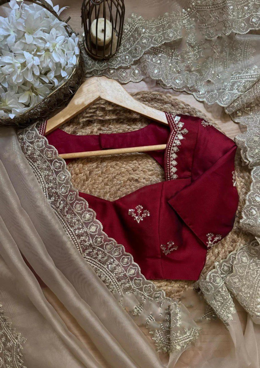 Close-up of a maroon blouse with gold embroidery and a draped beige organza saree with a delicate gold sequence border, set against a rustic background.
