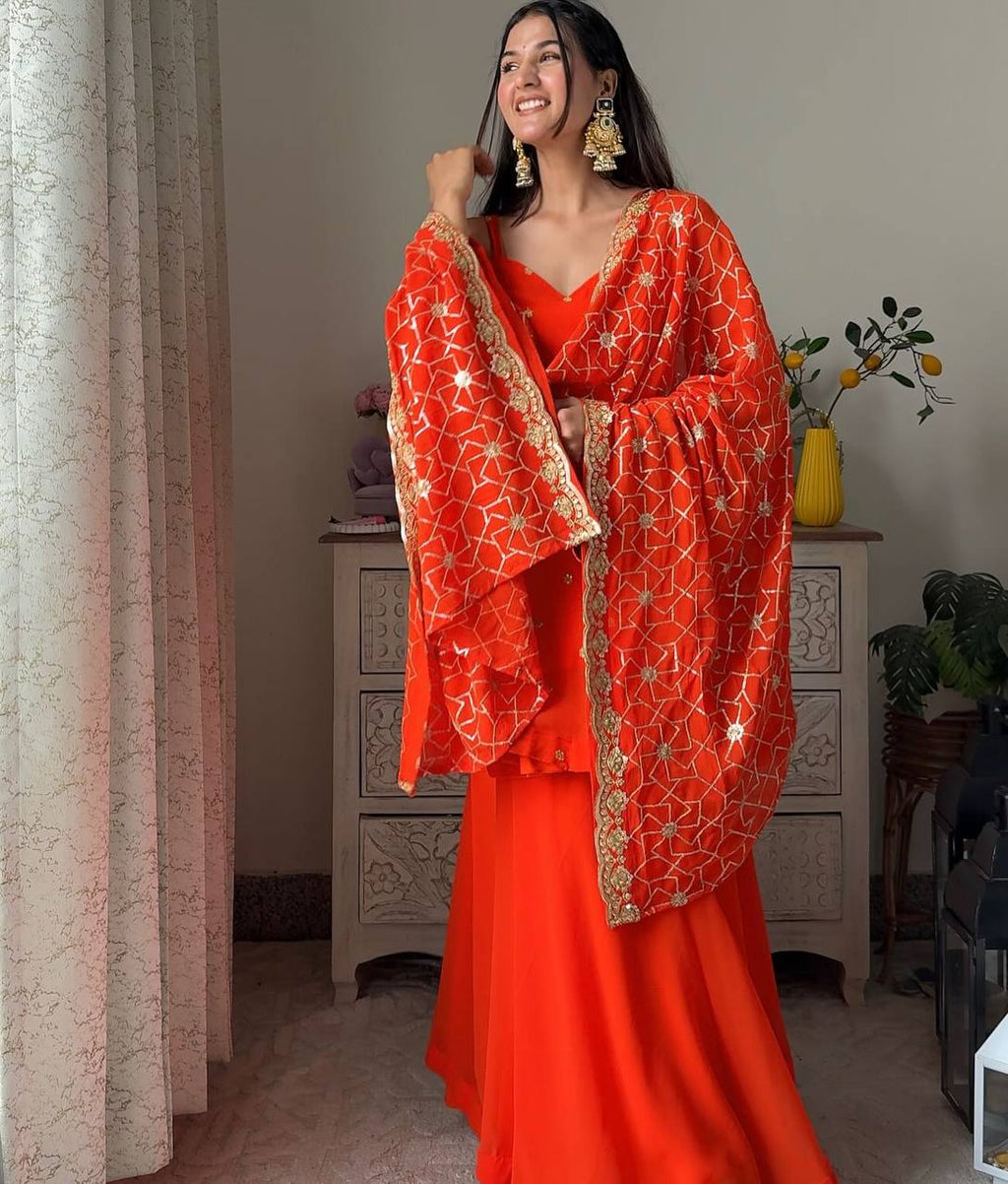 Woman smiling in radiant orange faux georgette palazzo set with sequence work dupatta, full body shot