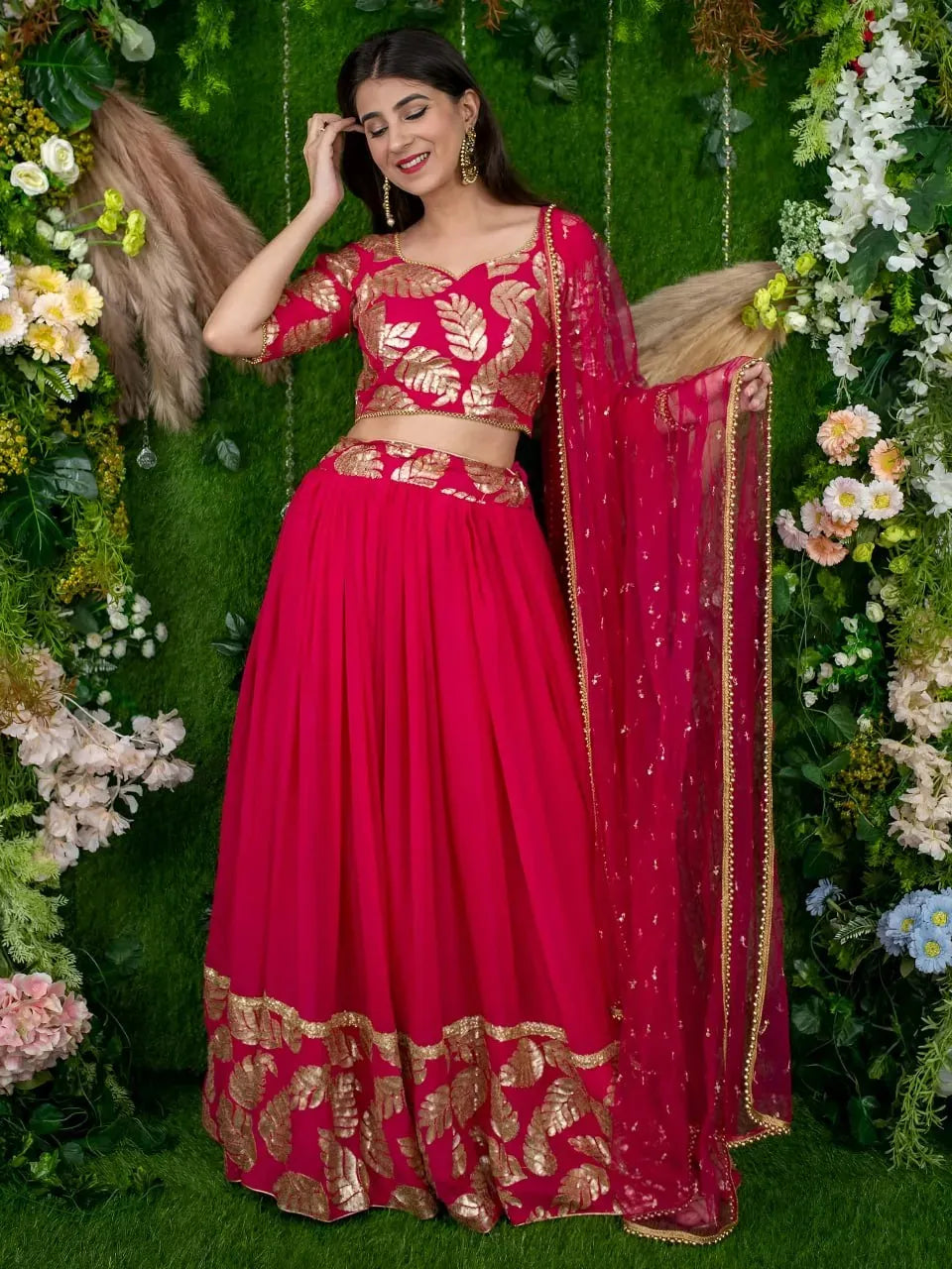 Model wearing pink designer lehenga with golden leaf embroidery against floral backdrop