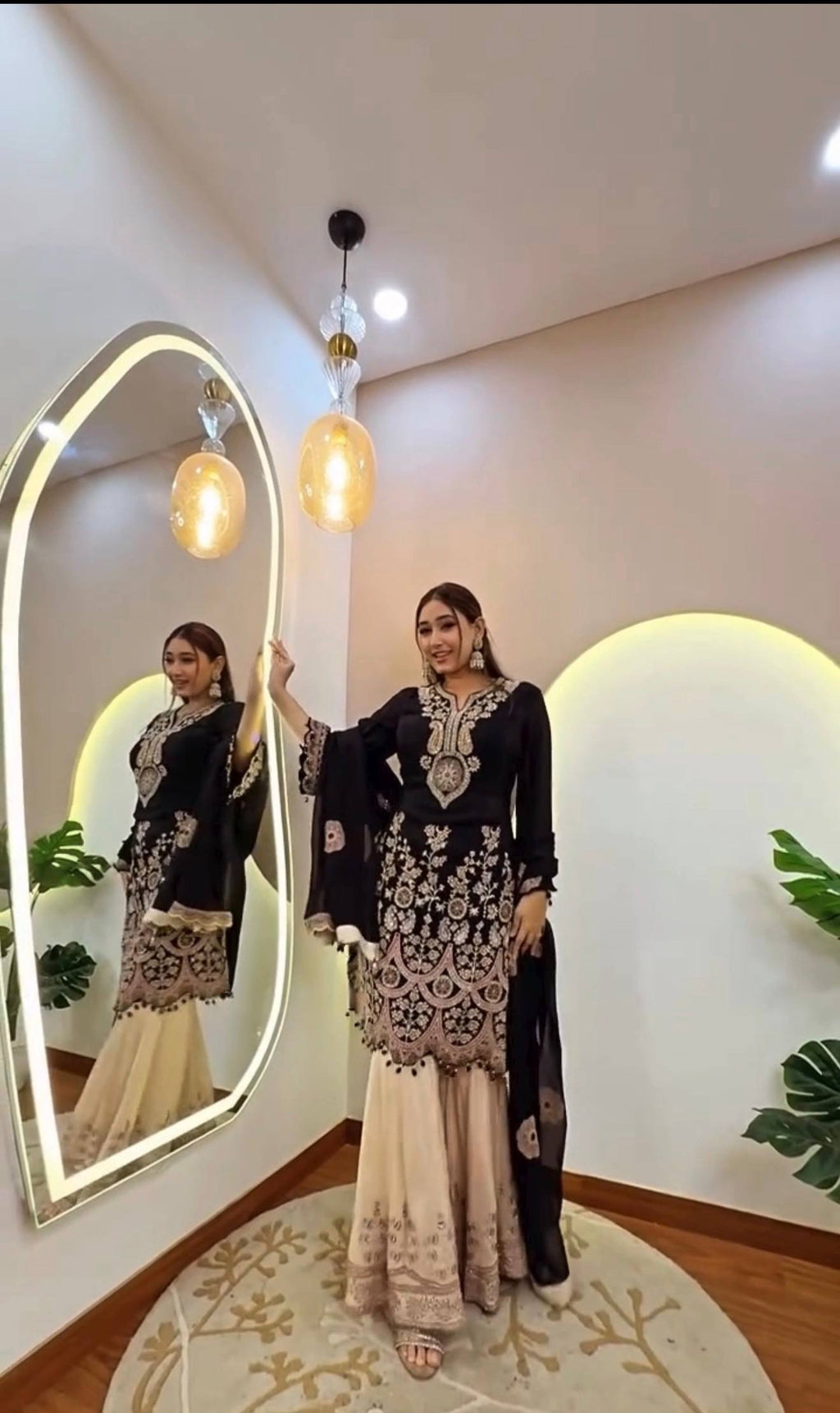 Model in black and gold embroidered ethnic wear, standing by a mirror.