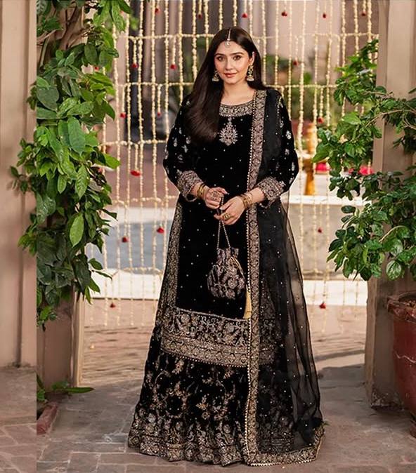 Model posing elegantly in a black designer velvet sharara suit with intricate gold embroidery and sequin work, perfect for festive occasions.