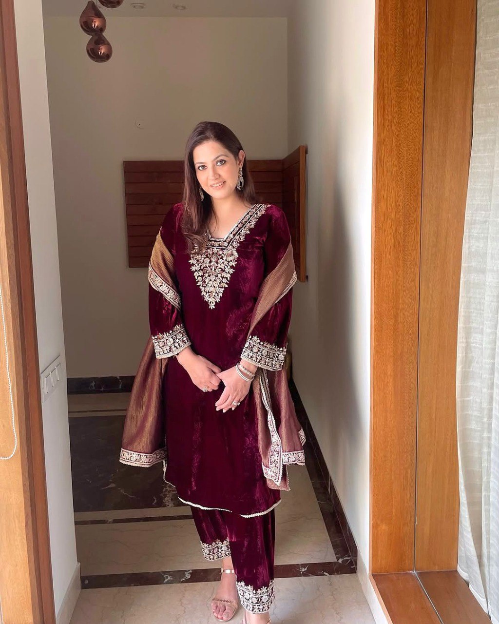 Woman wearing a maroon velvet suit with golden dupatta, full length, smiling elegantly.