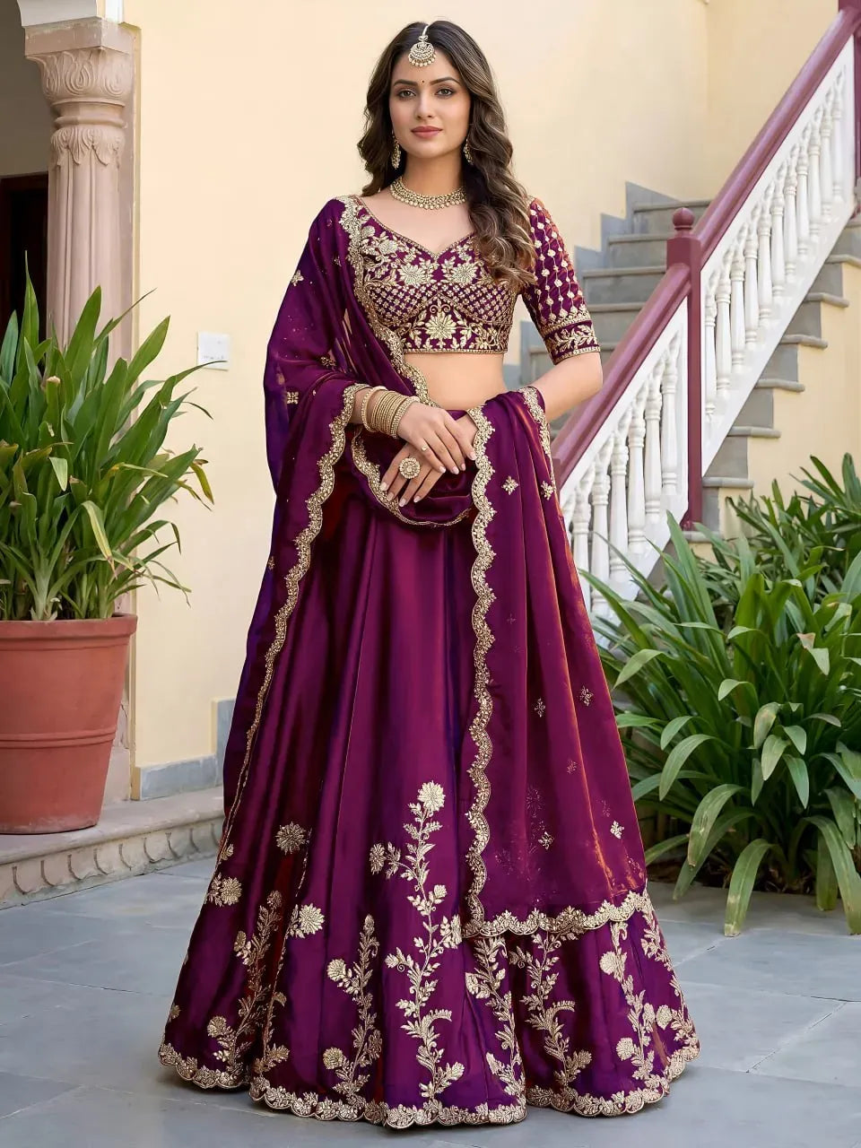 Model wearing wine embroidered lehenga choli with dupatta standing in front of stairs