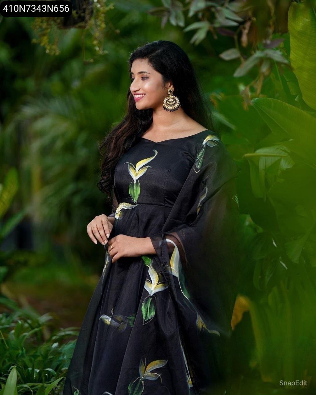 Model in black digital print organza gown, smiling, side profile in a garden setting.