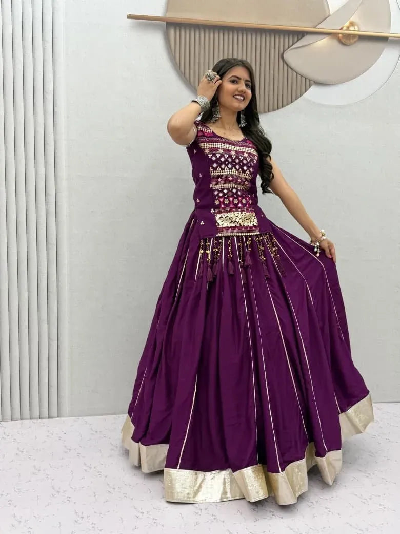 Woman in purple cotton lehenga choli with mirror hand work standing against a grey textured wall