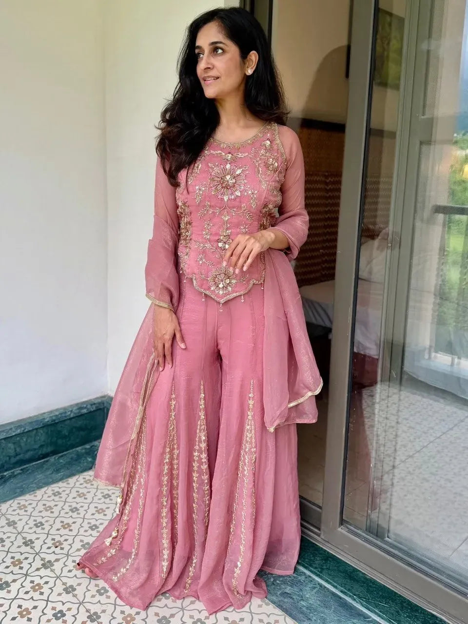 Model in a pink silk embroidered sharara set standing by a glass door looking aside
