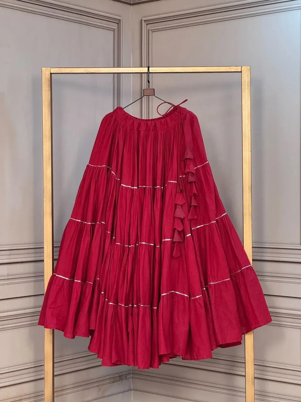 Maroon kora cotton flared lehenga skirt with gold trim layers displayed on a hanger