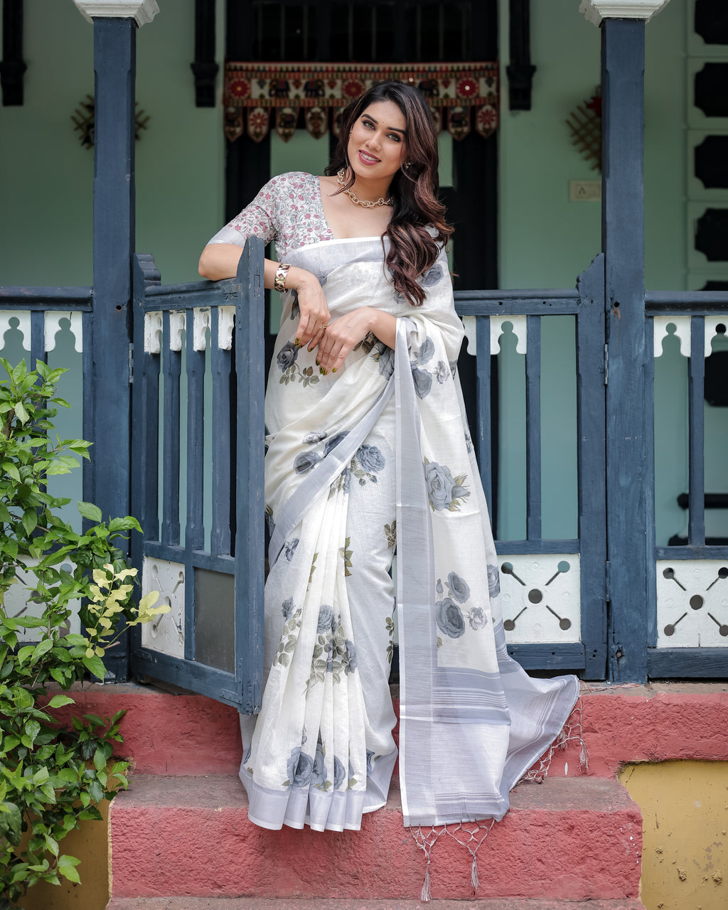 Woman posing in elegant white pure linen saree with grey floral prints and tassels, front view.