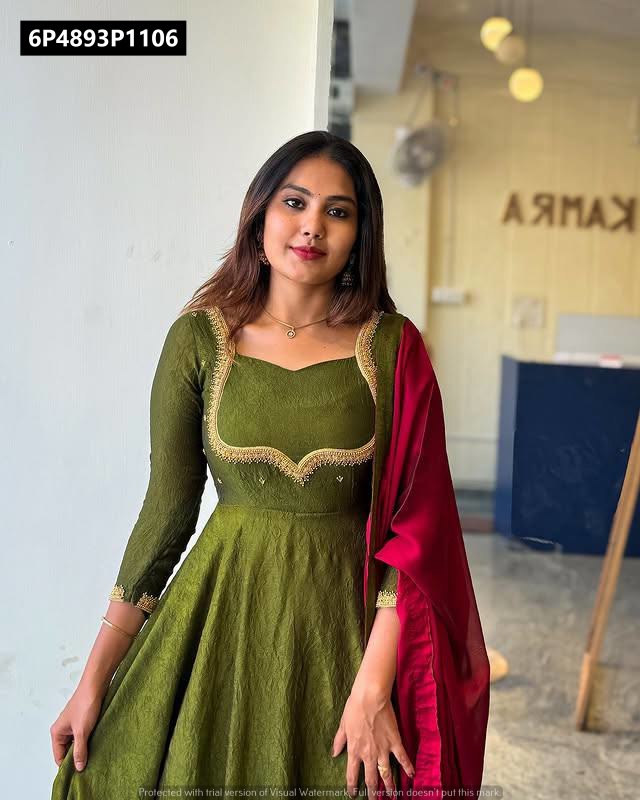 Full body shot of a woman in an olive green embroidered Anarkali gown with a maroon dupatta, posing indoors.