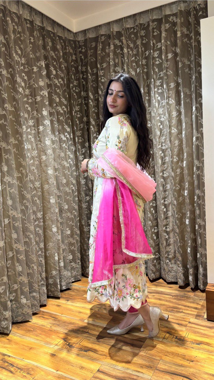 Woman posing in off-white embroidered kurti set with pink dupatta, side view.