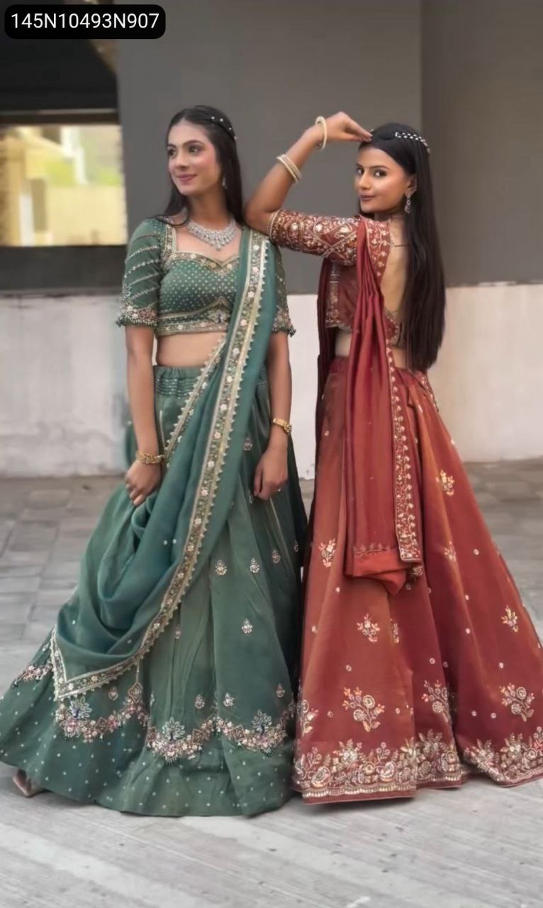 Two models in matching embroidered Chinon lehengas, one in emerald green and one in rustic red.