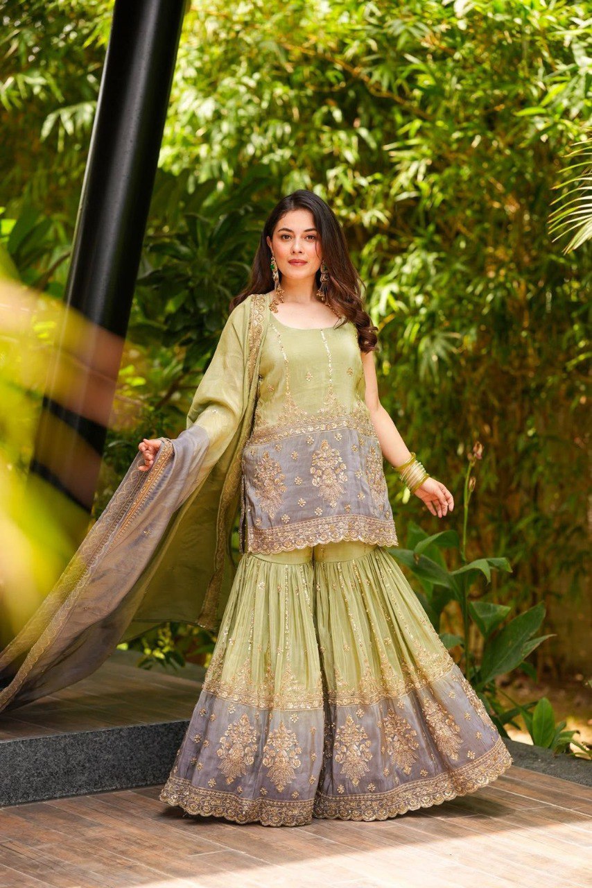 Woman posing in an elegant sage green and grey shaded Chinon sharara set with intricate embroidery and sequins, outdoor setting.