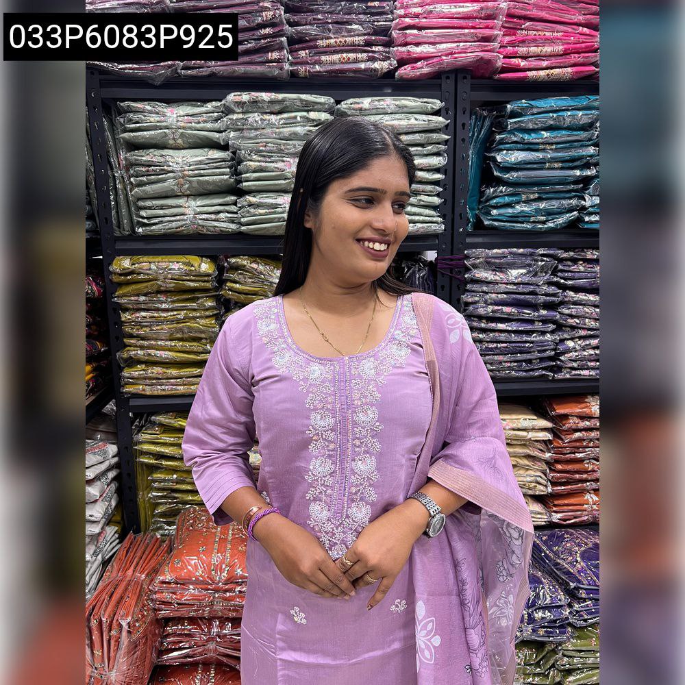 Woman in a lavender/purple outfit, smiling with long hair against a background of textile shelves.