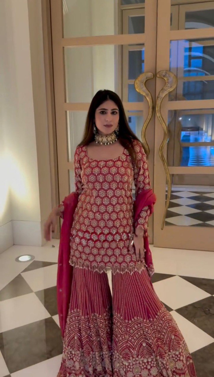 Woman posing gracefully in crimson embroidered sharara set with sequin work and dupatta, full view