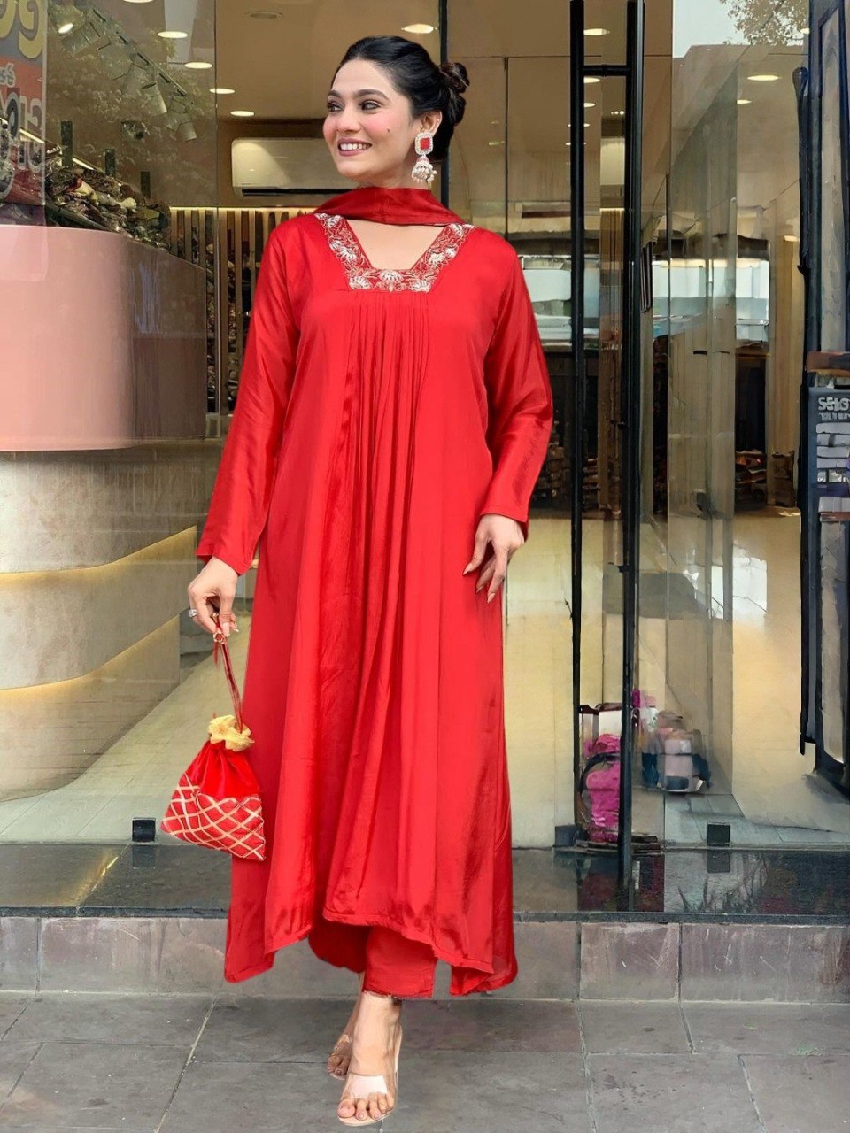 Elegant woman smiling in a full shot of the red embroidered flared kurta set with a matching pouch.