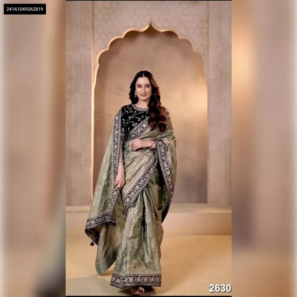 Beautiful woman gracefully posing in a sage green embroidered moss chiffon saree with a black velvet blouse, full-body front view.