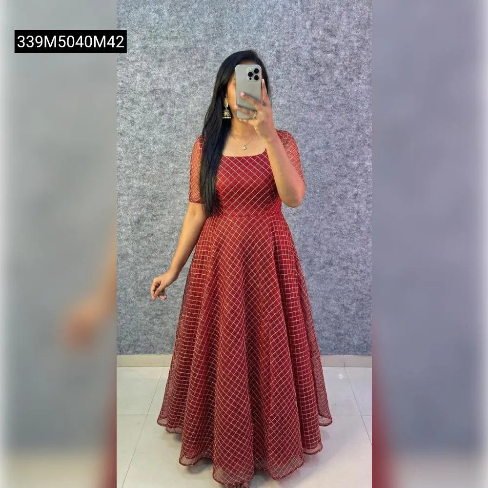 Model wearing a TRENDBUY Deep Red net frock with golden coding work, full length, standing against a grey wall, holding a phone.