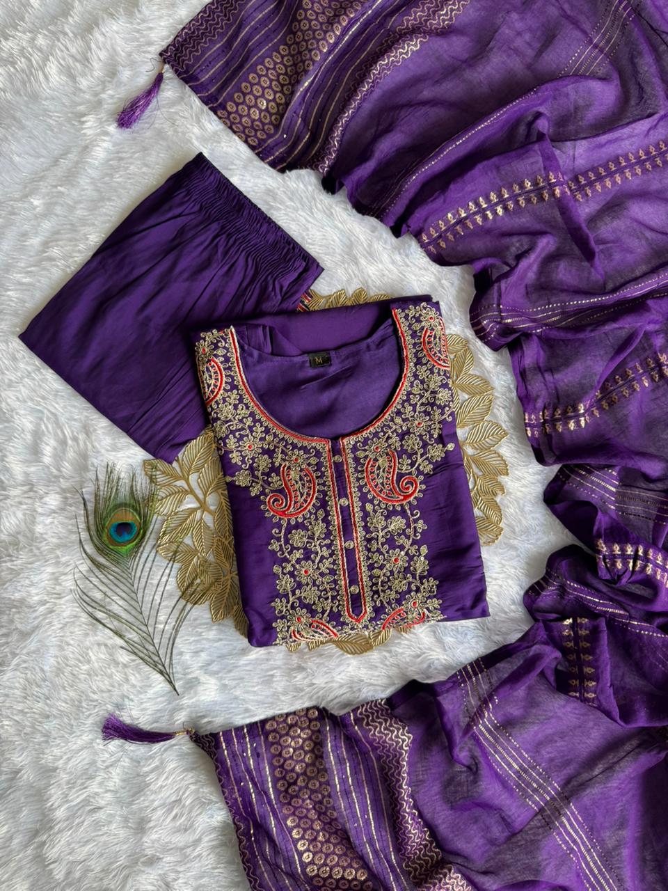 Overhead flat lay of the purple kurti set with embroidery, pant, and zari dupatta, on a white textured surface.