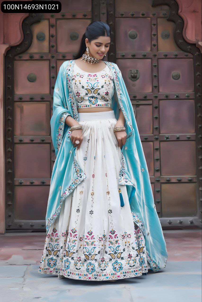 Full body shot of a model wearing an off-white embroidered tissue silk lehenga choli with an aqua blue dupatta, standing front-facing against a traditional door.
