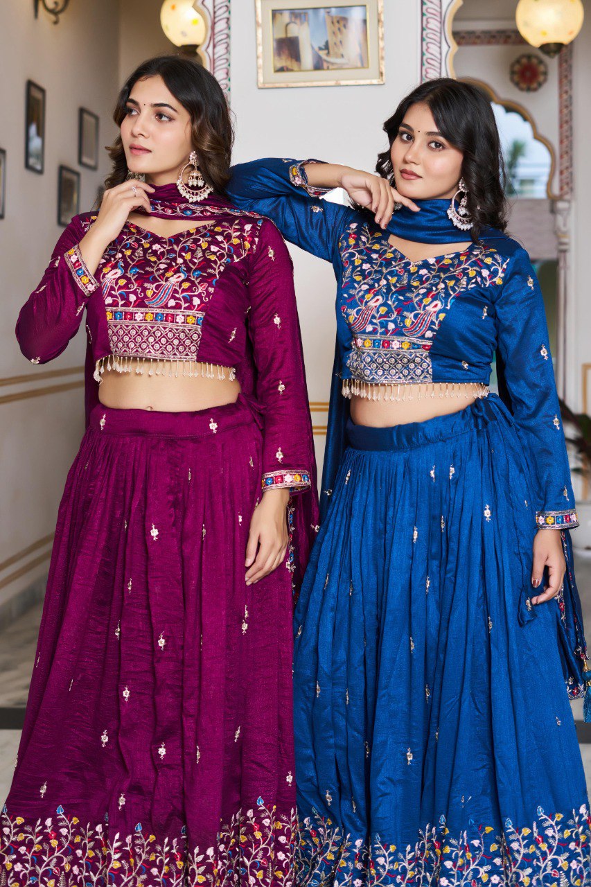 Two women posing in embroidered Vichitra Silk Lehenga Cholis, one in magenta, one in royal blue.