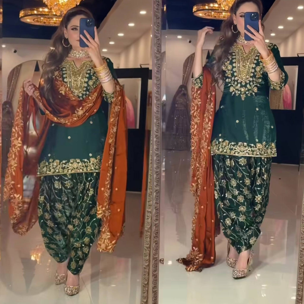 Woman in emerald green Chinon silk dhoti salwar suit with rust dupatta, full body shot.