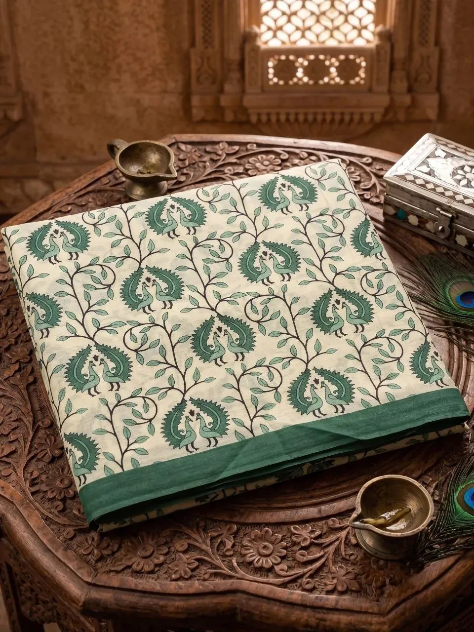 Folded green peacock and vine print cotton Kalamkari saree on carved wooden table